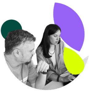 A black and white photo of a man and a woman collaborating while looking at a laptop. The man, on the left, is pointing towards the screen as if explaining something. The woman, on the right, is looking down at the screen. The image is cropped into a stylized circular shape with abstract graphic overlays in dark green, purple, and neon yellow.