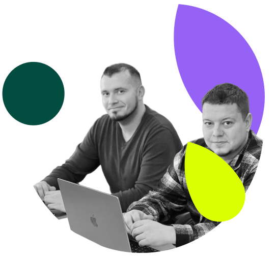 A greyscale image showing two men sitting at a desk with a laptop, both looking at the camera. The man in the foreground wears a plaid shirt, while the man behind wears a dark sweater. The image is decorated with abstract shapes in purple, dark green, and lime green.