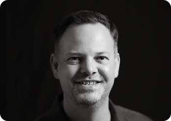 Black and white image of a man (Anthony, CEO at Systemseed) smiling.