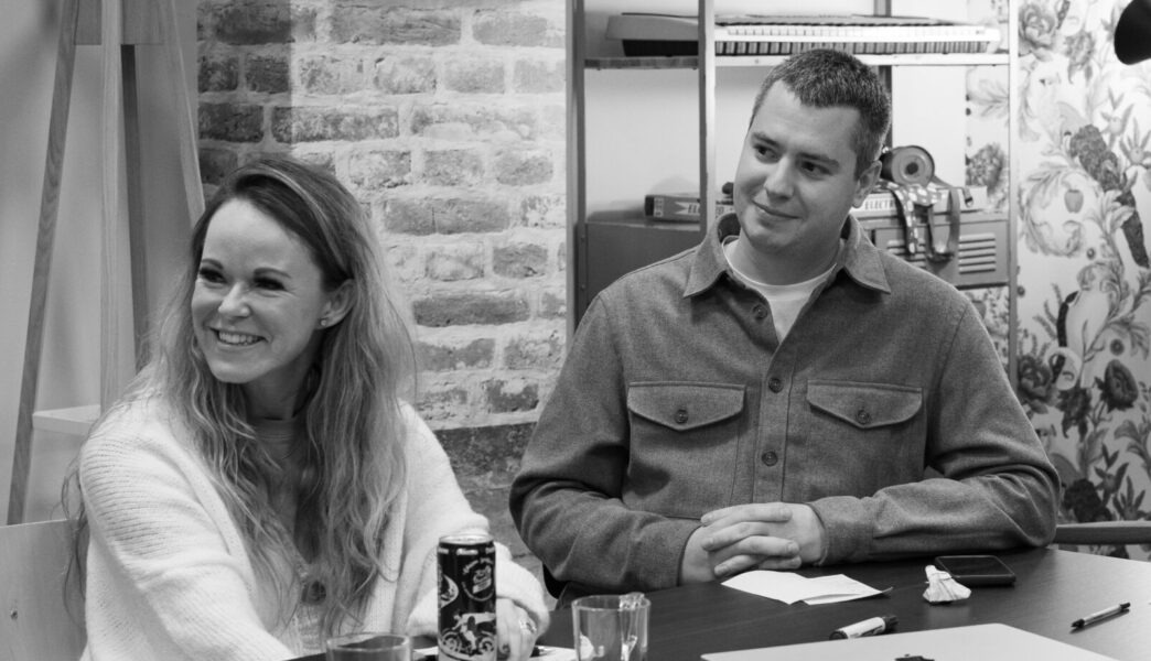 Black and white image of a man and a woman sitting at a table, smiling and engaged in conversation or a meeting.