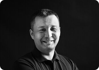 Black and white image of a man (Elaman, Technical Lead at Systemseed) smiling.