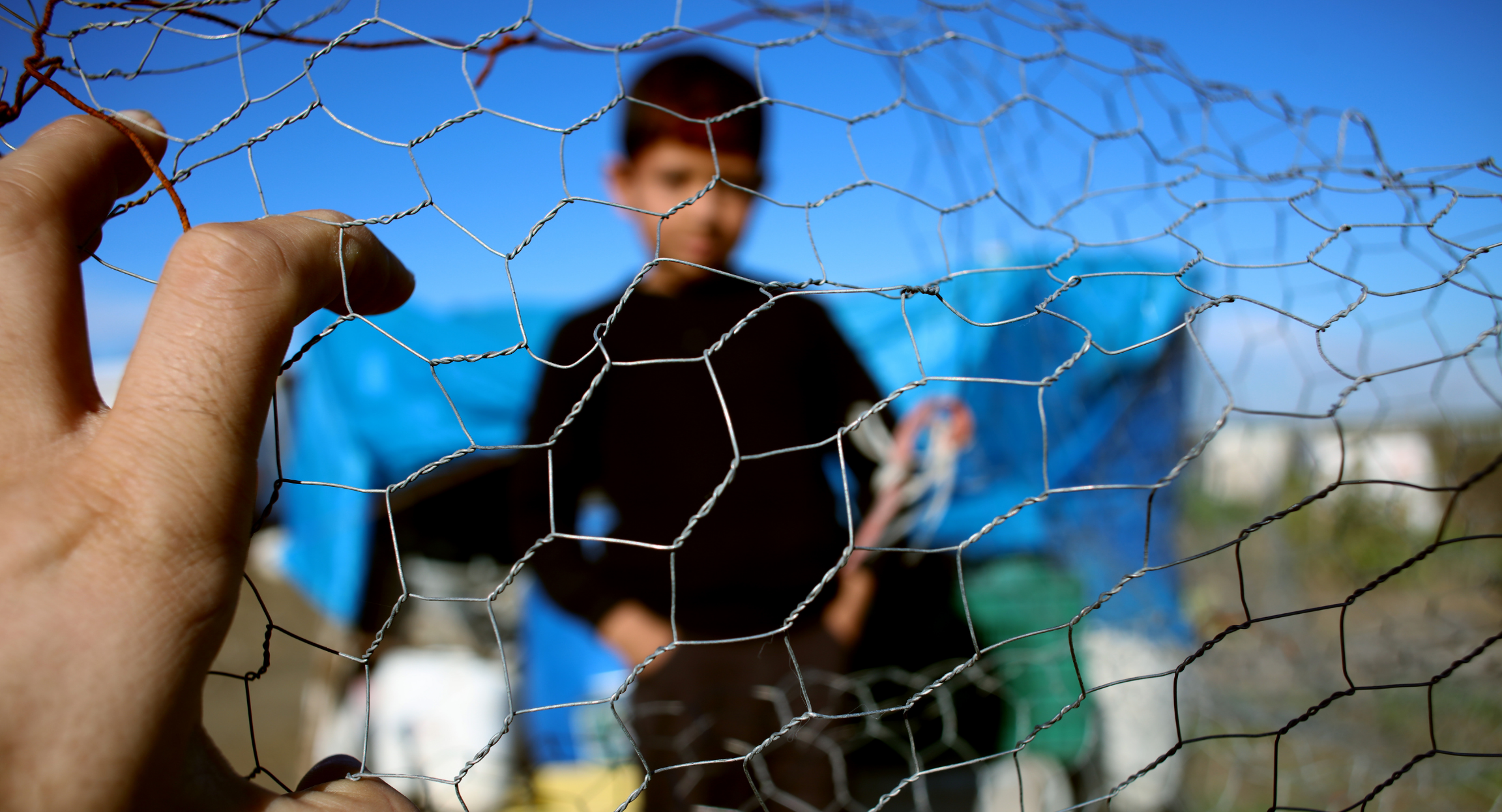 Boy at refugee camp looking through fence
