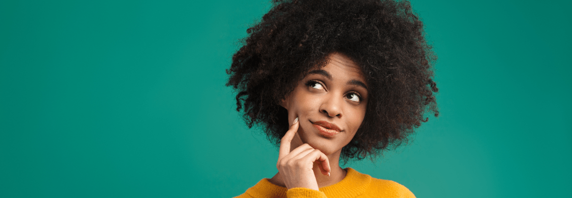 A young black woman with natural hair wears a yellow jumper and looks thoughtfully upwards