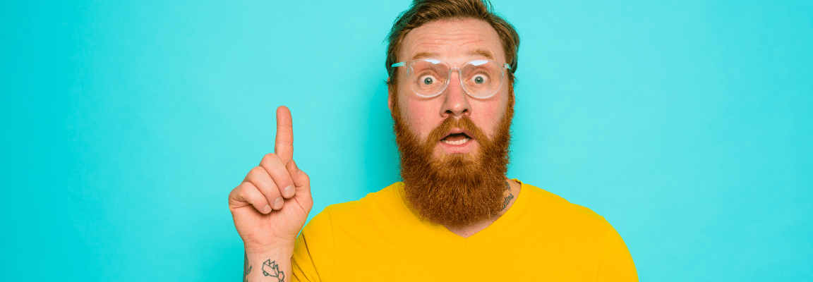 A white man with a beard in a yellow t-shirt and glasses looks like he has an idea