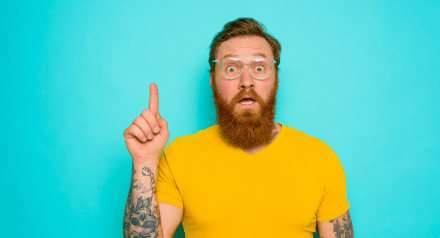 A white man with a beard in a yellow t-shirt and glasses looks like he has an idea
